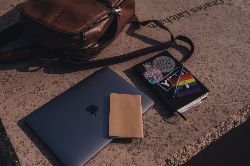 A Mac and a notebook on a concrete bench outside at a public park.